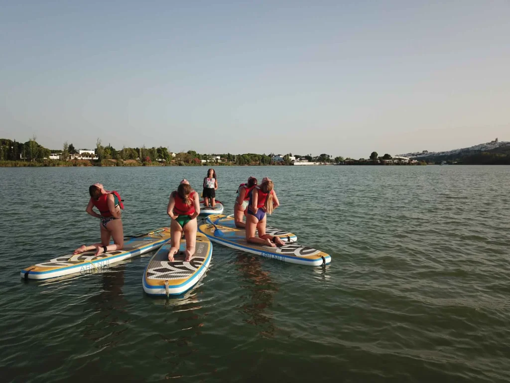varias chicas practicando yoga sobre paddle en el lago de arcos